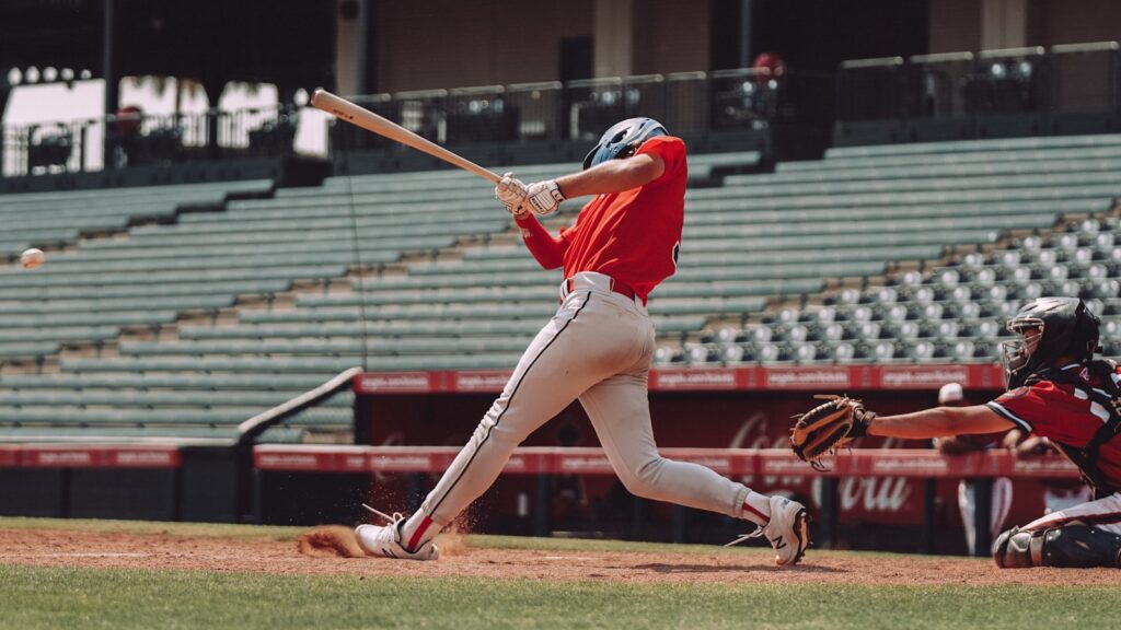 woman in red jersey shirt and white shorts holding baseball bat